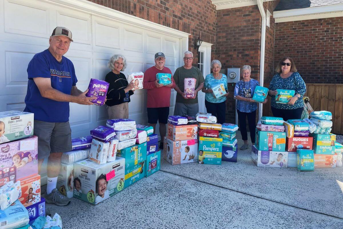Men and women holding and surrounded by packages of baby diapers